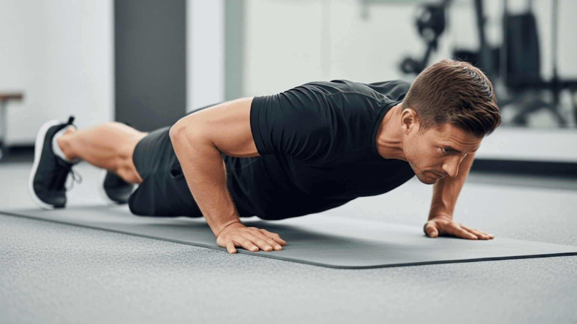 A man performs a push-up with a straight body, hands slightly wider than shoulders, elbows bent, and core engaged on a gym mat.