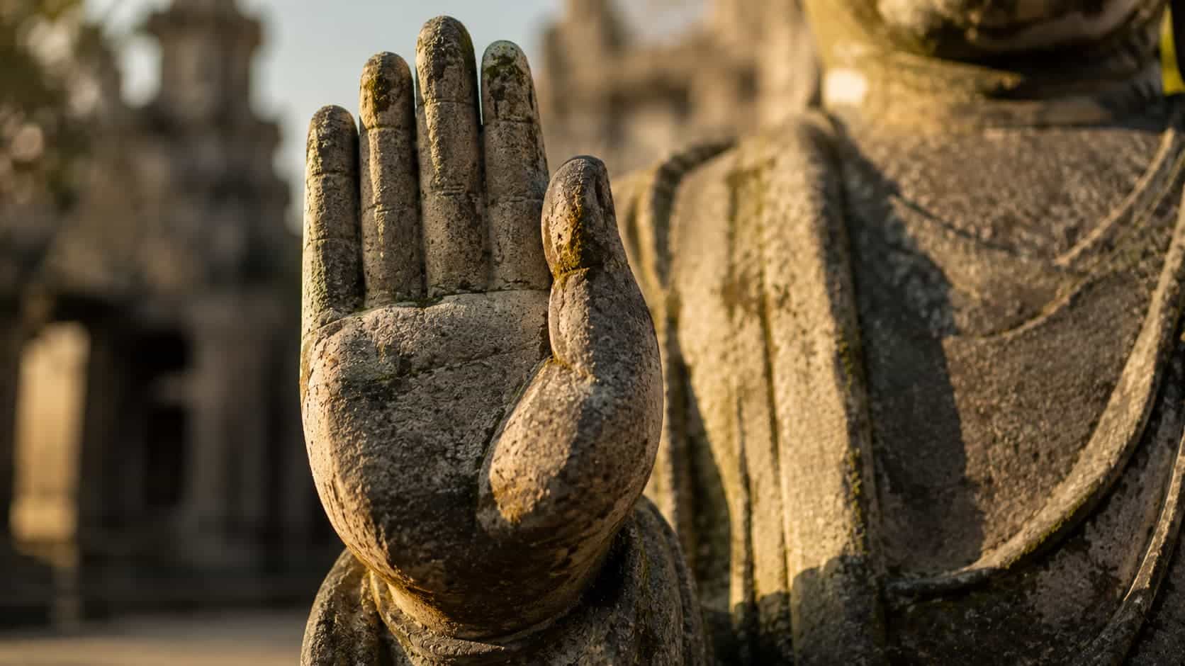 Close-up of a weathered stone Buddha statue's raised right hand showing the Abhaya Mudra gesture of fearlessness.