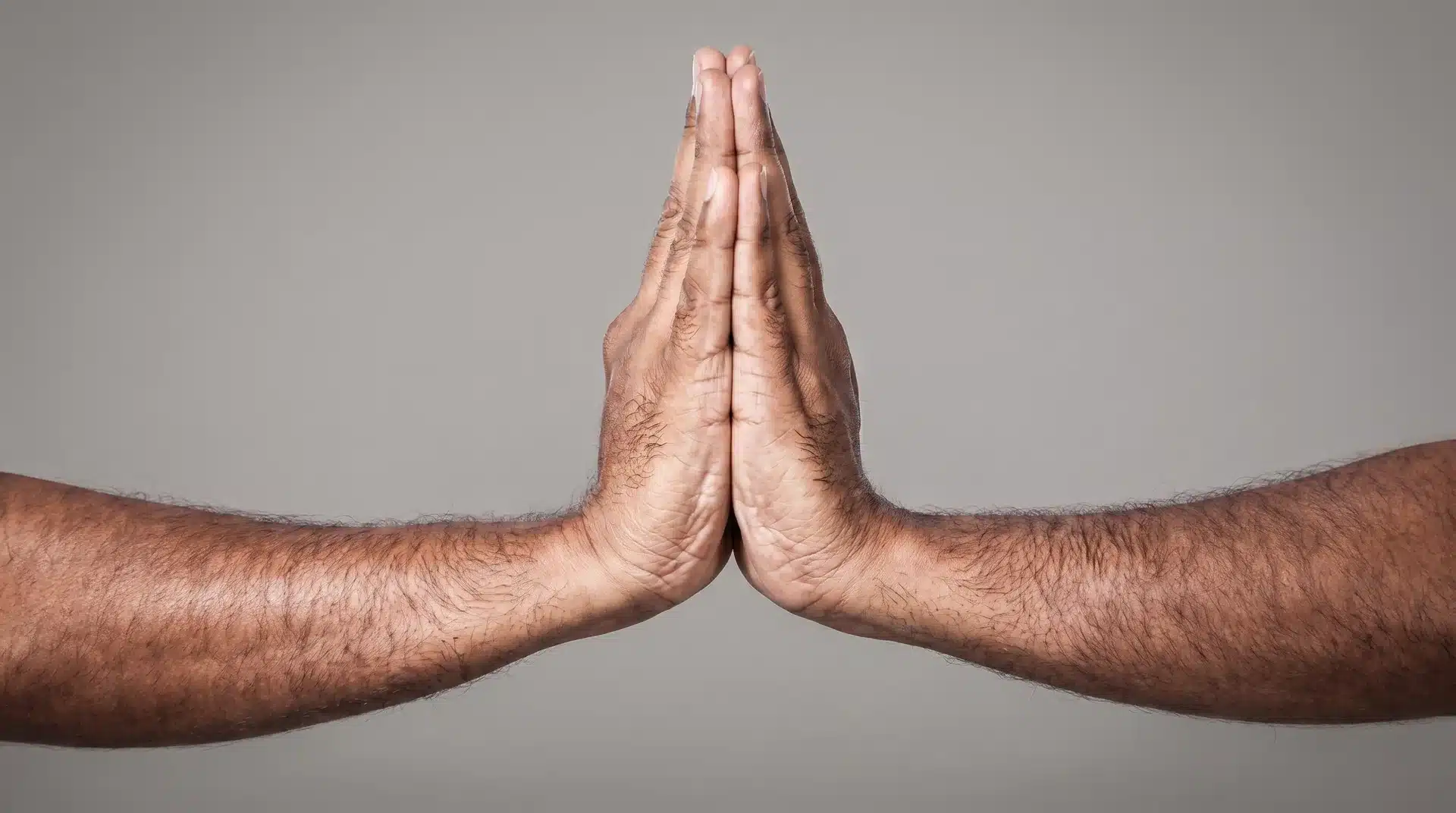 Two arms coming together from opposite sides to press the palms firmly together in front of a plain background, forming the Anjali Mudra prayer position.