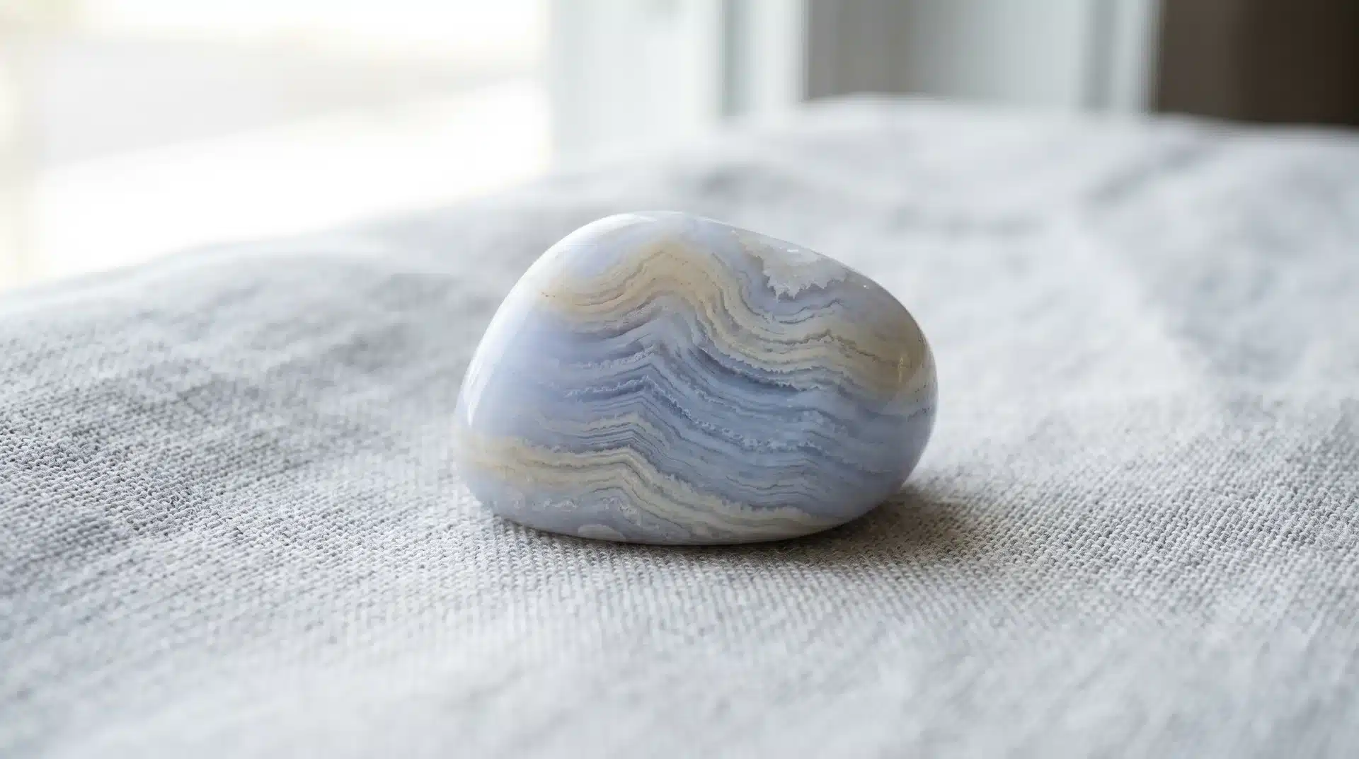 A polished blue lace agate stone with light blue and white bands resting on a light gray fabric surface.