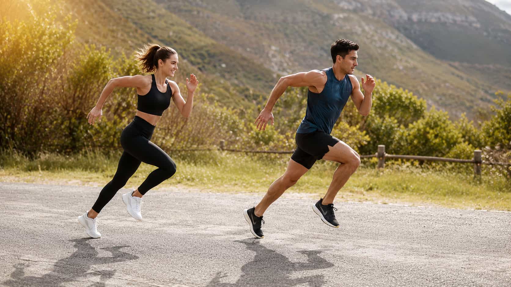A man and a woman in athletic wear running side-by-side along an outdoor paved path with mountains visible in the background.