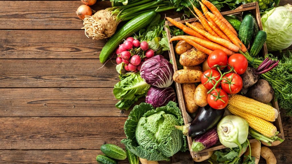 Fresh low FODMAP vegetables including carrots, tomatoes, cucumber, cabbage, eggplant, and potatoes on a wooden table.