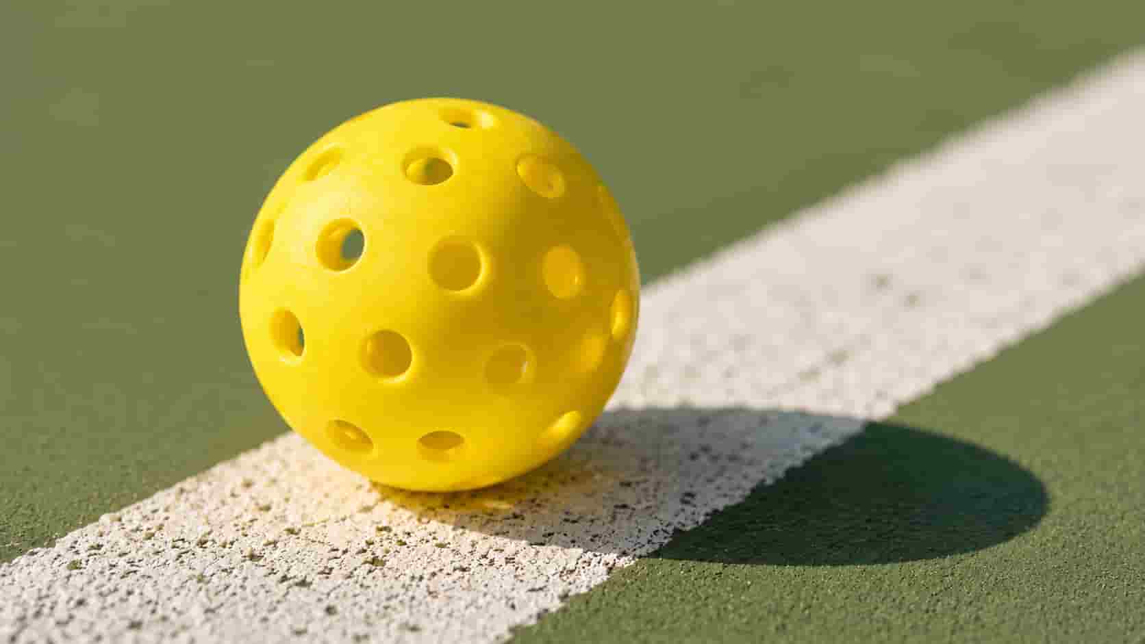 A bright yellow perforated pickleball sitting on an outdoor court line.