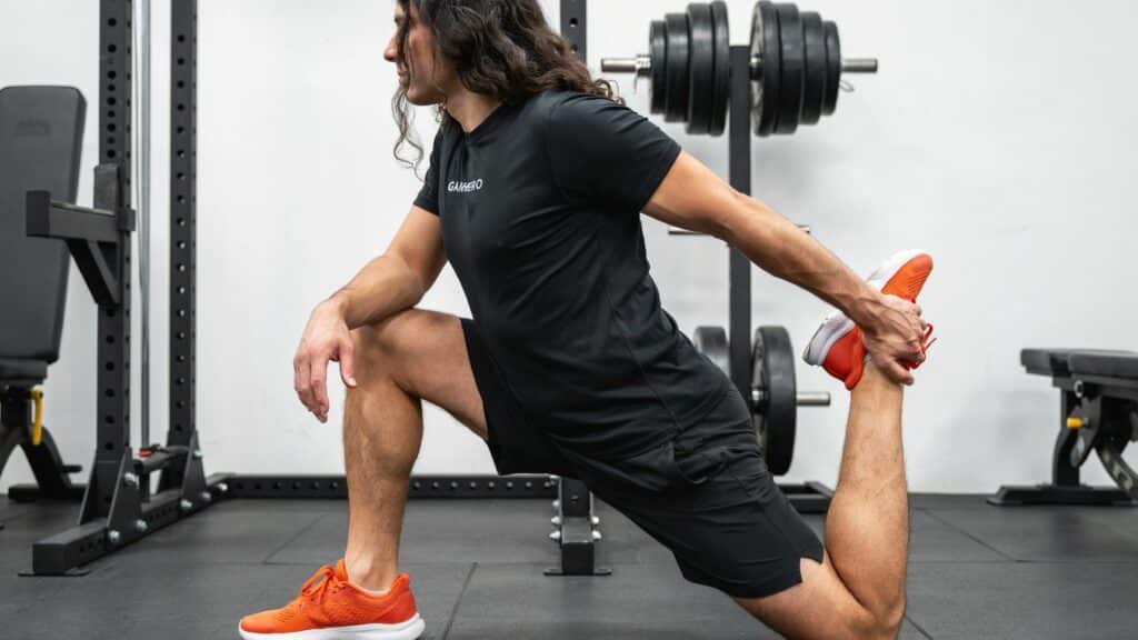 Man in a gym performing a deep kneeling quad stretch by holding his back foot up toward his glutes.