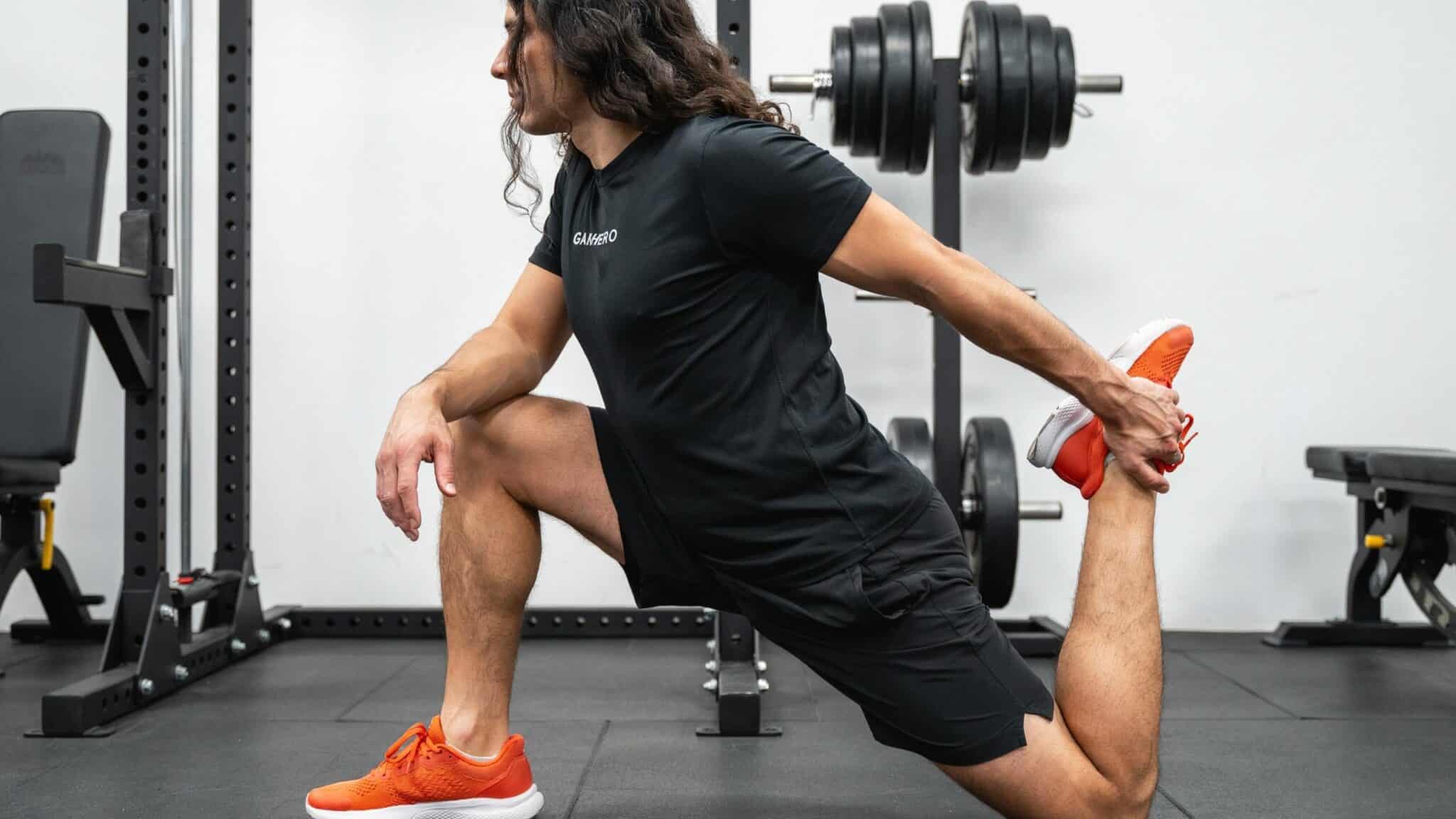 Man in a gym performing a deep kneeling quad stretch by holding his back foot up toward his glutes.