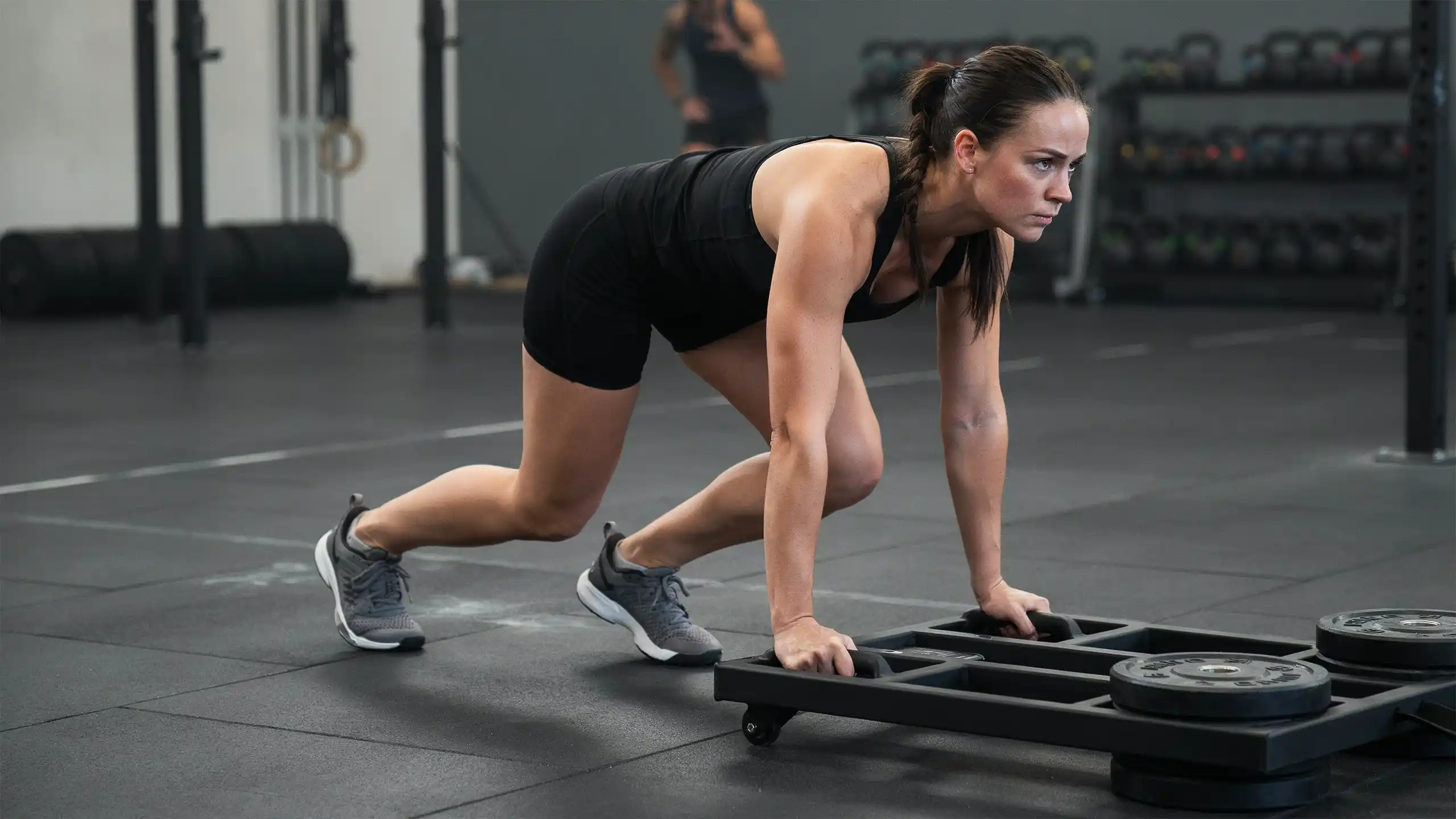 Female athlete performing a weighted sled push during HYROX training, demonstrating proper technique, strength, and controlled movement.