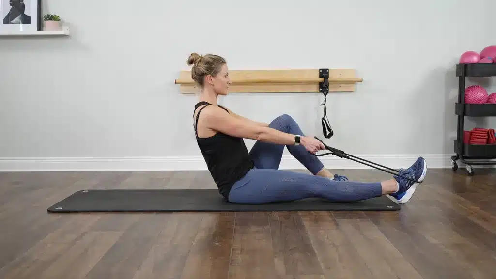 Woman on a yoga mat using a strap around her foot to perform a strap-assisted seated quad stretch.