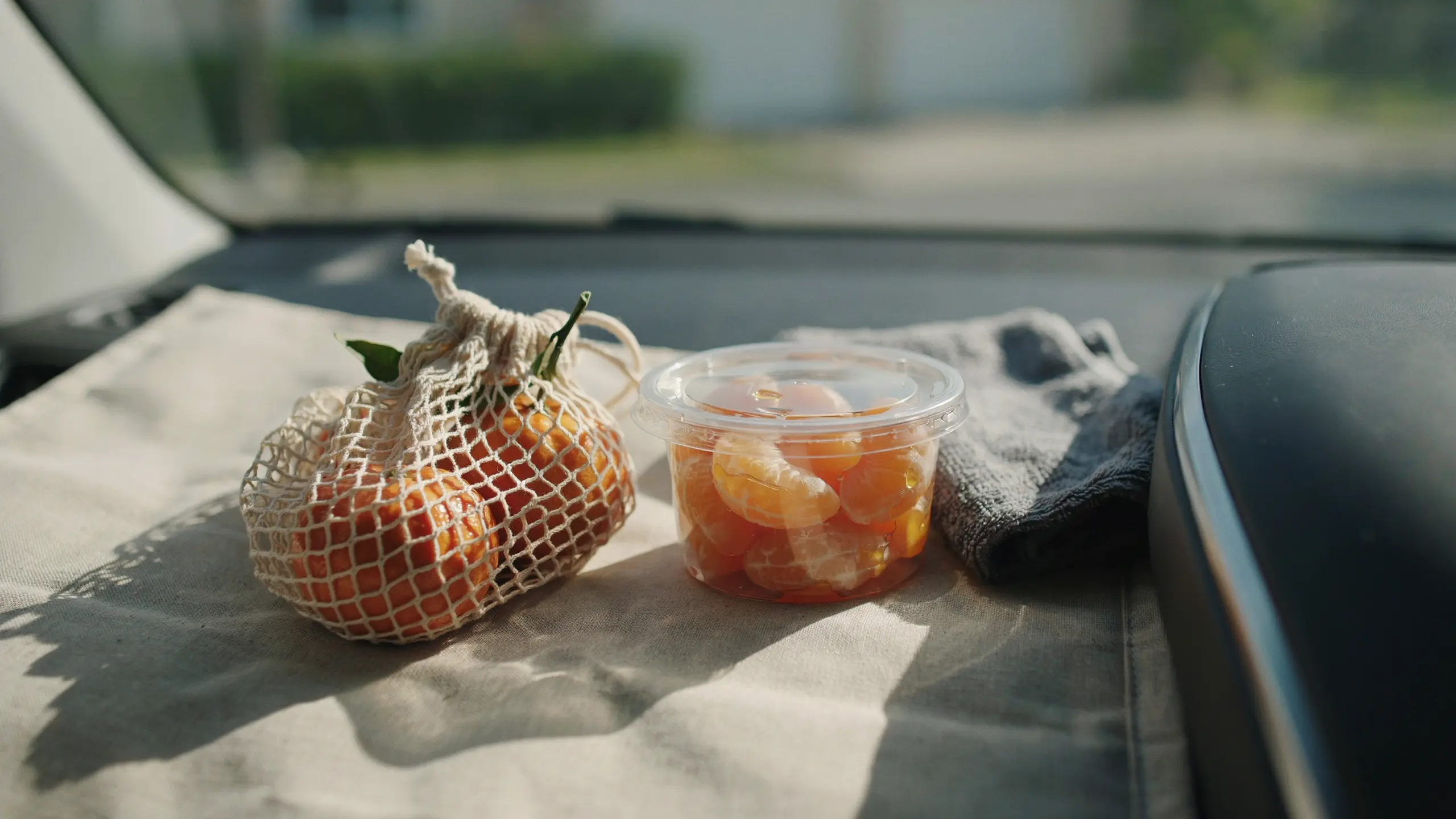 Peeled mandarins in a container with whole oranges packed for a road trip snack.