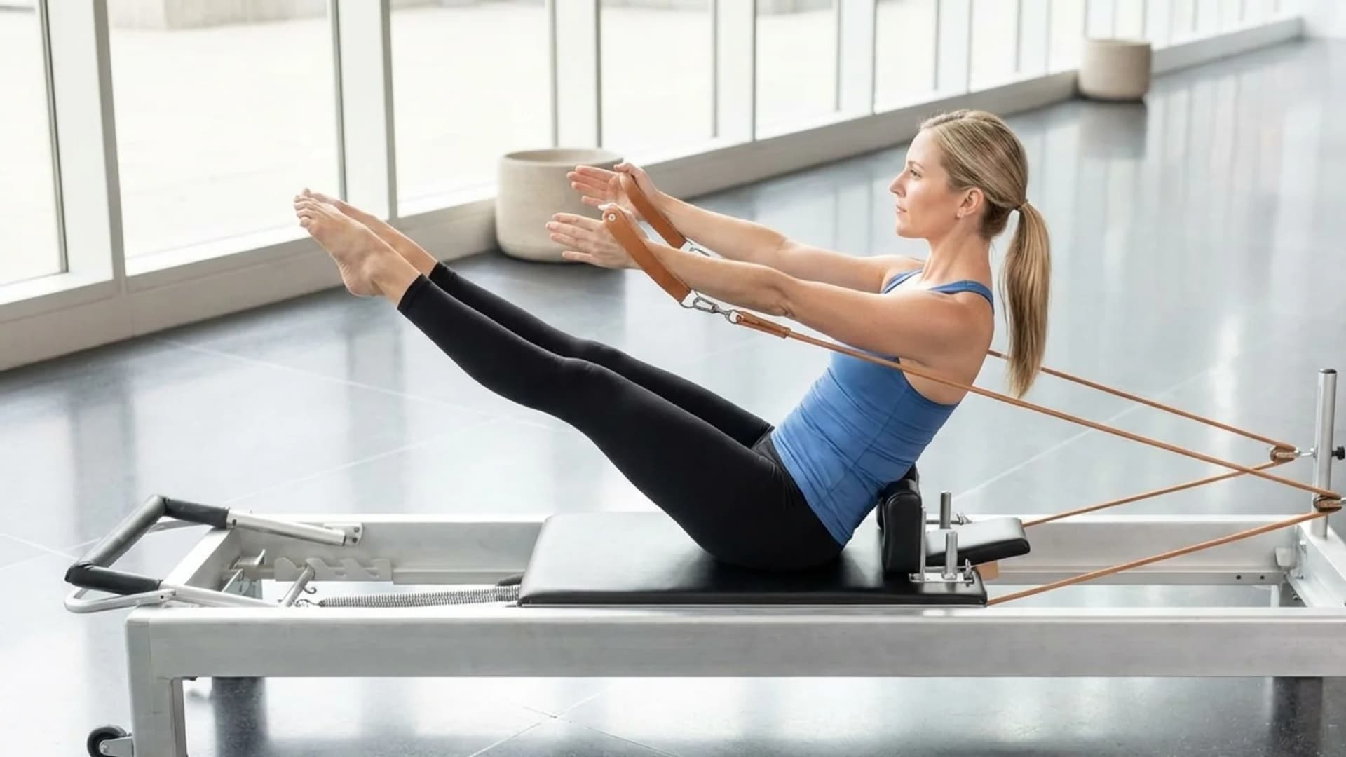Woman performing a Classical Pilates Teaser pose on a Reformer machine in a studio.